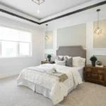 A cozy budget-decorated bedroom with white walls featuring warm textured bedding, a jute rug, rattan pendant light, and green indoor plants for a designer look on a budget