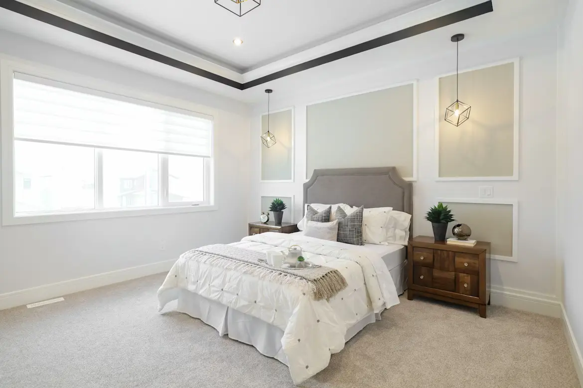 A cozy budget-decorated bedroom with white walls featuring warm textured bedding, a jute rug, rattan pendant light, and green indoor plants for a designer look on a budget